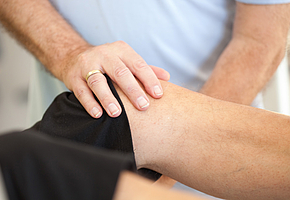 Die Hände eines Therapeuten, der einen Patienten am Knie behandelt.