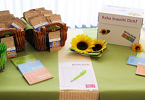 Auf einem Tisch stehen zwei Körbe mit kleinen Säckchen in denen Sonneblumensamen sind und ein Gefäß mit Kugelschreibern. Daneben liegen Postkarten der DEGEMED Aktion und eine Unterschriftenliste.